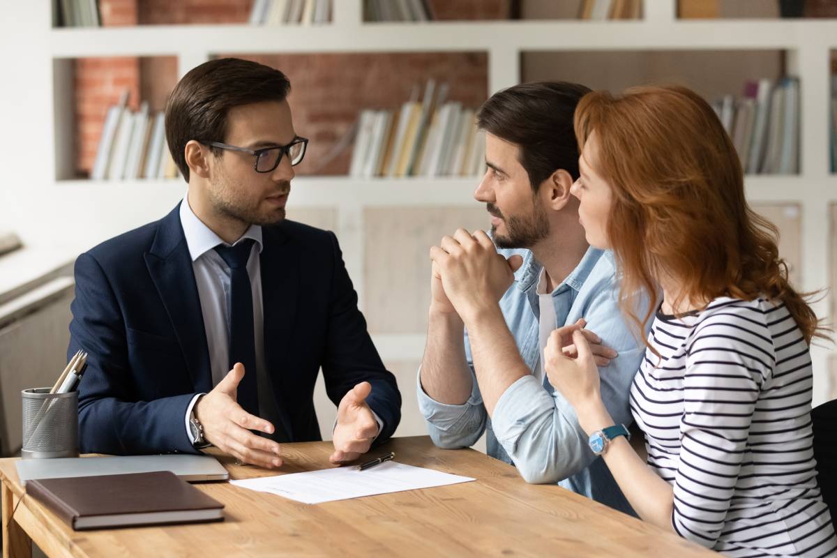 Request a consultation Financial advisor discussing documents with a couple at a table in a bright office